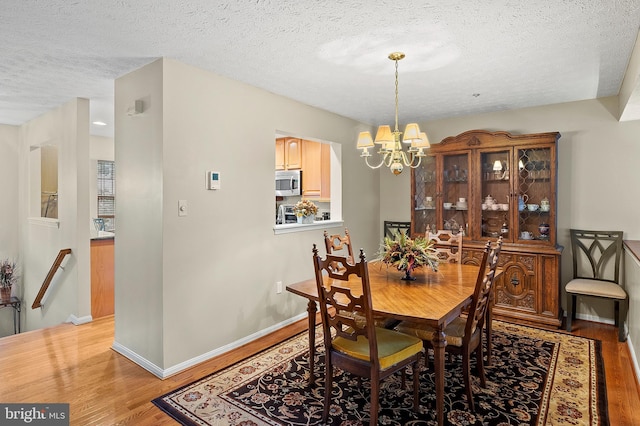 dining space featuring light wood-style flooring, a textured ceiling, a chandelier, and baseboards