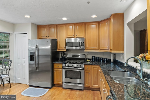 kitchen with stainless steel appliances, a sink, light wood-style floors, dark stone counters, and brown cabinets