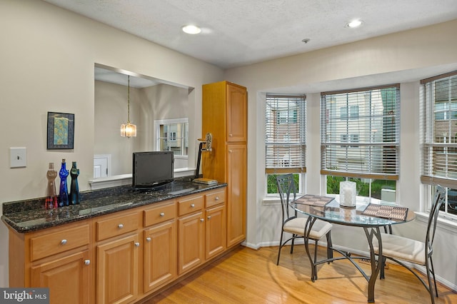 kitchen featuring light wood-style floors, dark stone countertops, baseboards, a textured ceiling, and brown cabinetry