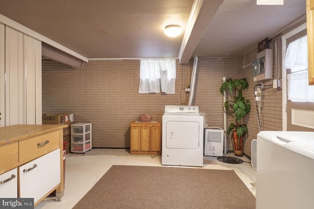 laundry area with brick wall, healthy amount of natural light, washing machine and clothes dryer, and cabinet space