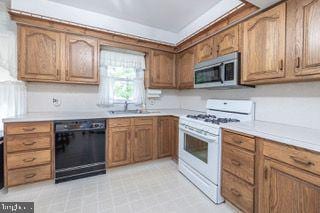 kitchen featuring gas range gas stove, black dishwasher, stainless steel microwave, a sink, and brown cabinetry