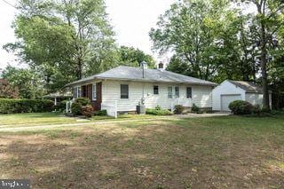 rear view of property with an outdoor structure, a lawn, and a detached garage