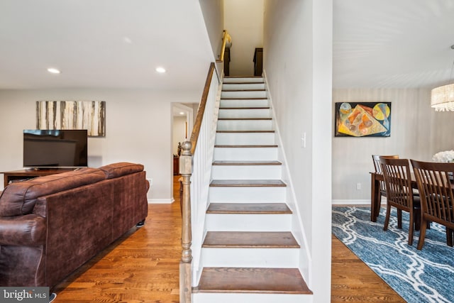stairway featuring wood finished floors, baseboards, recessed lighting, and a chandelier