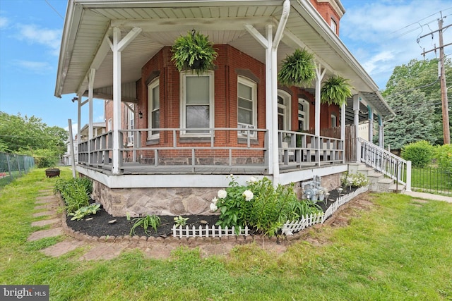 view of side of home with a porch, brick siding, and a lawn