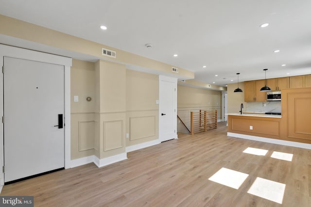 unfurnished living room with light wood finished floors, recessed lighting, wainscoting, and a sink