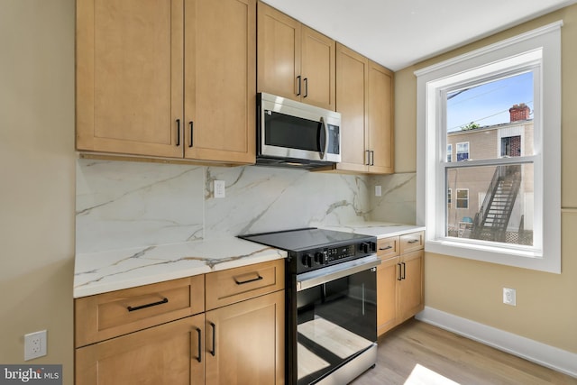 kitchen with stainless steel microwave, electric range, light wood-style flooring, baseboards, and decorative backsplash