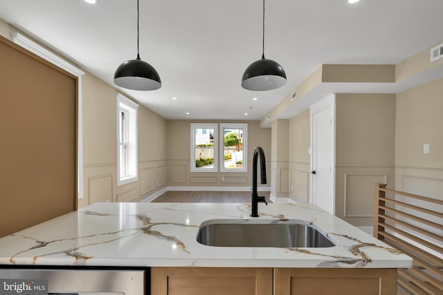 kitchen with a sink, a decorative wall, open floor plan, stainless steel dishwasher, and wainscoting
