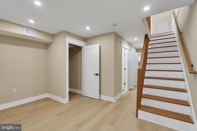 finished below grade area featuring light wood-type flooring, recessed lighting, baseboards, and stairs