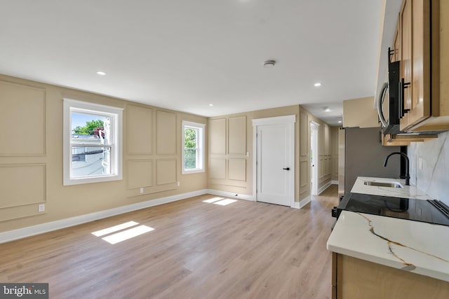 kitchen with a sink, a decorative wall, light wood-style floors, light countertops, and baseboards