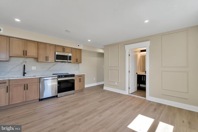 kitchen with appliances with stainless steel finishes, a sink, light countertops, light wood-style flooring, and decorative backsplash