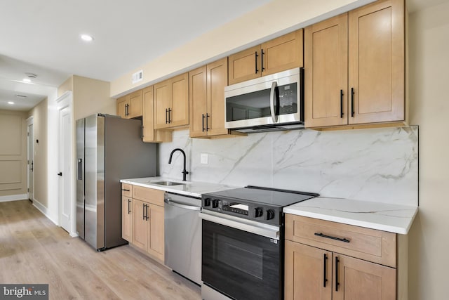 kitchen featuring appliances with stainless steel finishes, a sink, light brown cabinetry, light wood-style floors, and backsplash