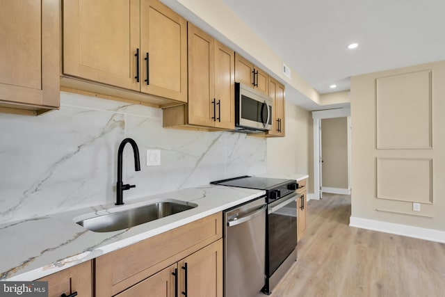 kitchen with appliances with stainless steel finishes, a sink, light wood finished floors, backsplash, and light stone countertops