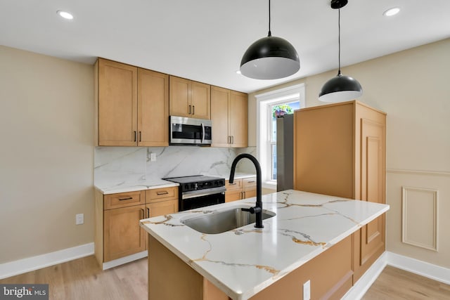 kitchen with appliances with stainless steel finishes, a sink, light wood-style flooring, tasteful backsplash, and light stone countertops