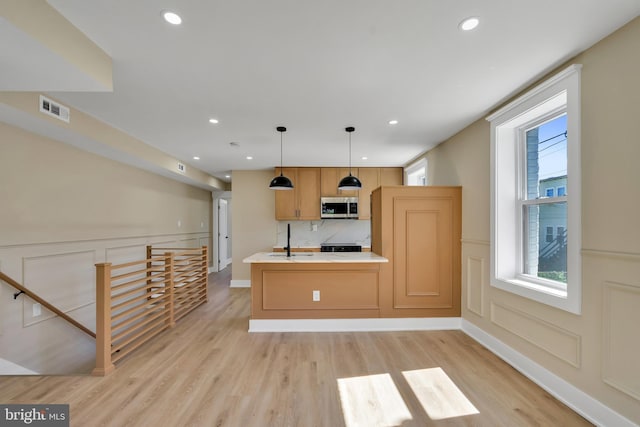 kitchen with stainless steel microwave, a decorative wall, light wood-style floors, light countertops, and a sink