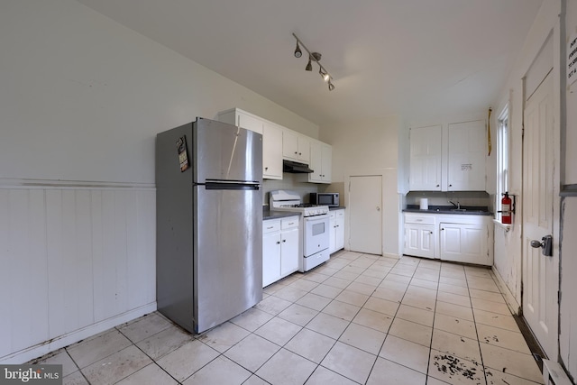 kitchen featuring appliances with stainless steel finishes, under cabinet range hood, dark countertops, white cabinets, and wainscoting