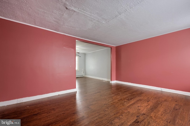 spare room featuring a textured ceiling, wood finished floors, ornamental molding, and baseboards