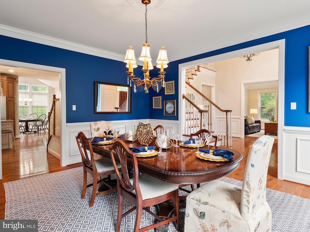 dining room with stairs, a chandelier, plenty of natural light, wood finished floors, and wainscoting