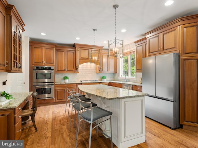 kitchen featuring appliances with stainless steel finishes, brown cabinets, a chandelier, light wood-style floors, and recessed lighting