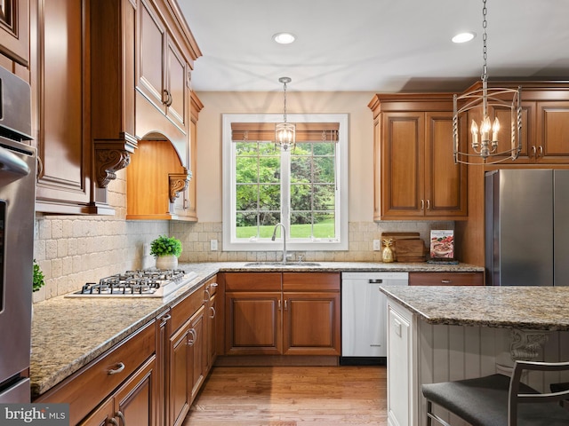 kitchen with a sink, appliances with stainless steel finishes, a chandelier, brown cabinets, and recessed lighting