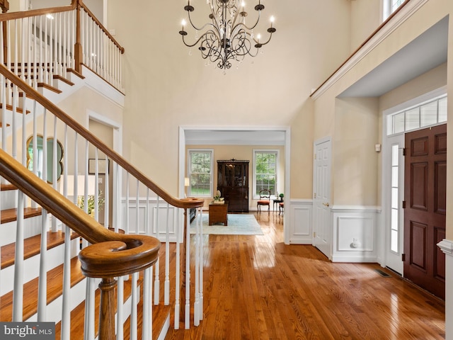 foyer entrance featuring stairs, a chandelier, hardwood / wood-style floors, a high ceiling, and a wainscoted wall