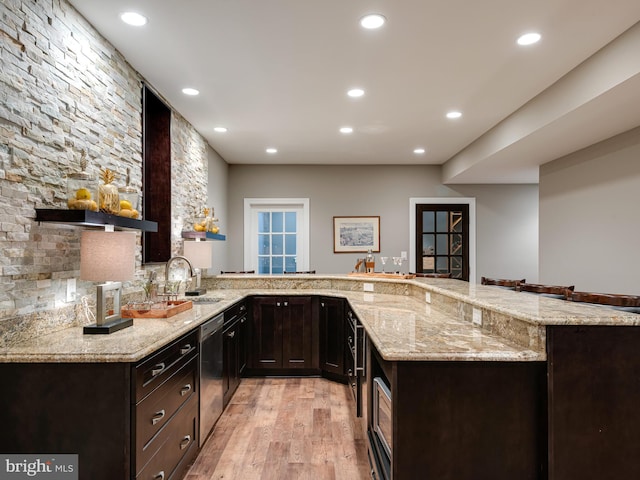 kitchen featuring a sink, stainless steel dishwasher, light wood-style flooring, dark brown cabinets, and light stone countertops