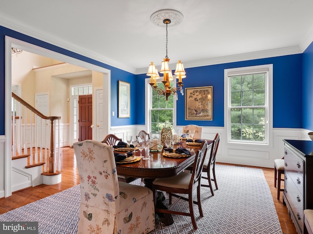 dining space featuring a chandelier, stairs, wainscoting, wood finished floors, and crown molding