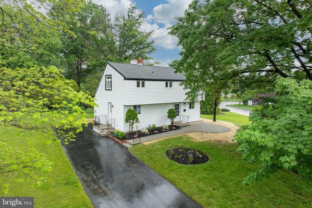 colonial home with a chimney, a front yard, driveway, a shingled roof, and a patio