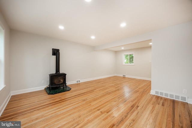 unfurnished living room with a wood stove, wood finished floors, recessed lighting, and baseboards
