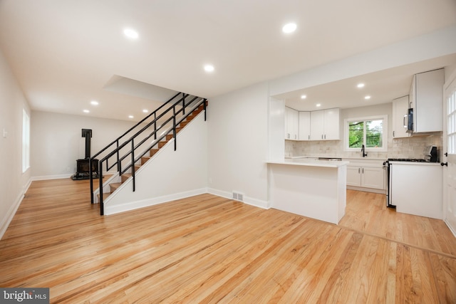 kitchen featuring stainless steel gas range, light wood-style flooring, tasteful backsplash, white cabinets, and recessed lighting