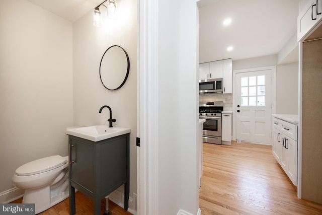 bathroom with wood finished floors, toilet, vanity, and decorative backsplash