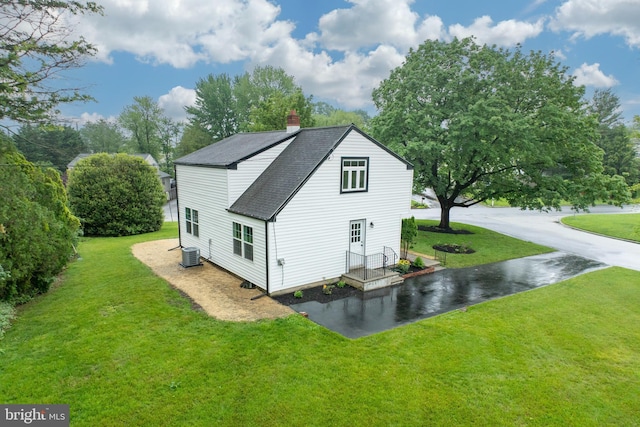 view of home's exterior featuring central AC unit, a shingled roof, a chimney, and a lawn