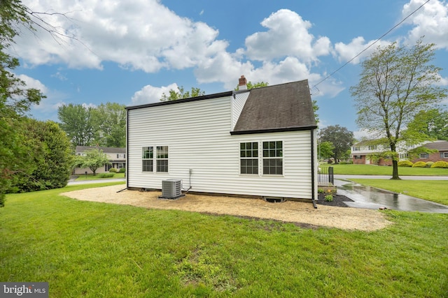 back of house featuring a lawn, central AC, a chimney, and a shingled roof