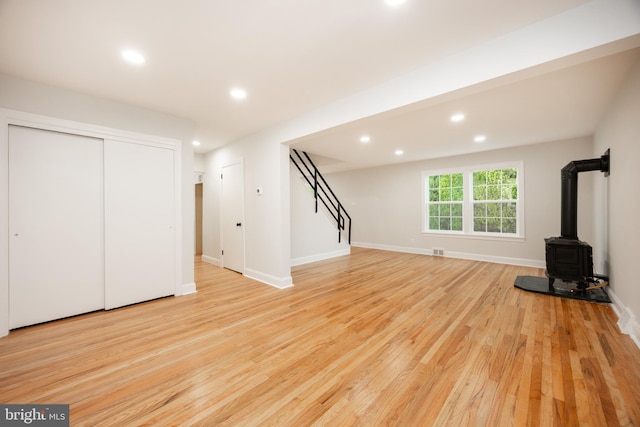 unfurnished living room with light wood-style floors, stairs, recessed lighting, a wood stove, and baseboards