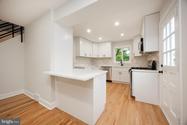 kitchen featuring appliances with stainless steel finishes, light wood-style floors, a peninsula, backsplash, and recessed lighting