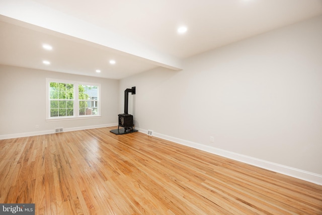unfurnished living room with a wood stove, light wood-style floors, recessed lighting, and baseboards