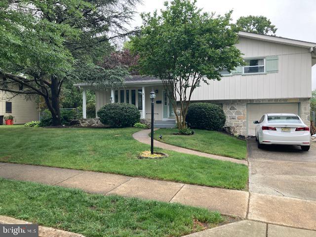 tri-level home with a garage, driveway, a front yard, and stone siding