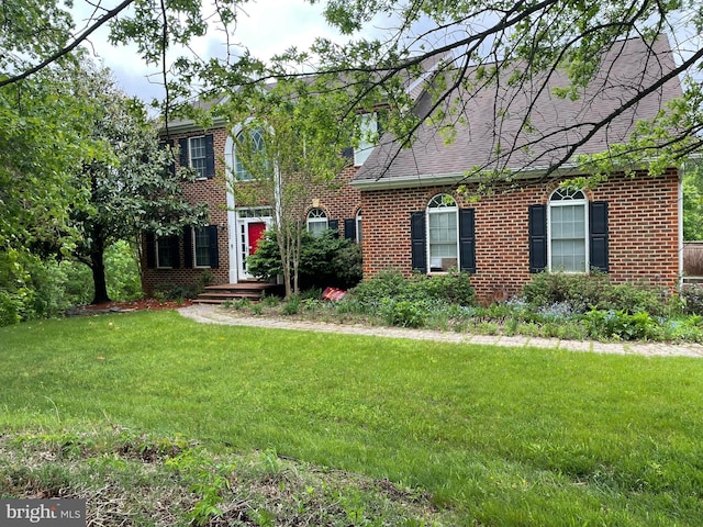 colonial-style house with brick siding, a front yard, and roof with shingles