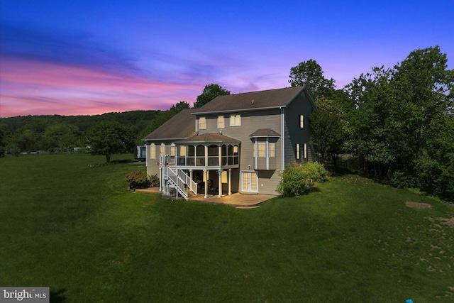 back of house at dusk featuring a patio area, a yard, a deck, french doors, and stairway