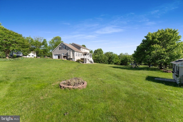 view of grassy yard with an outdoor fire pit, stairway, and a deck