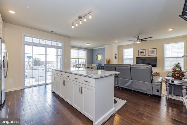 kitchen featuring dark wood-type flooring, a ceiling fan, plenty of natural light, light stone counters, and crown molding