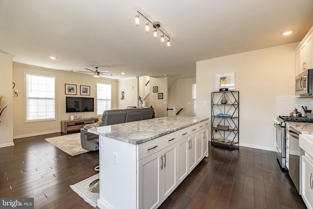 kitchen featuring appliances with stainless steel finishes, a center island, a ceiling fan, white cabinets, and dark wood-type flooring