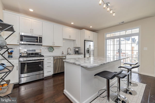 kitchen featuring appliances with stainless steel finishes, dark wood-style flooring, a breakfast bar, white cabinetry, and recessed lighting