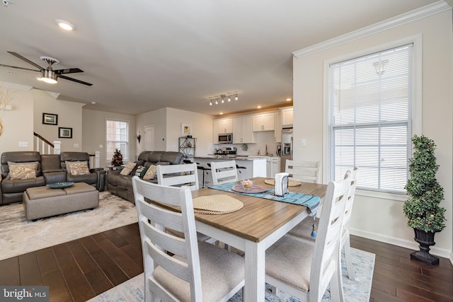 dining space featuring dark wood-style flooring, a ceiling fan, stairs, baseboards, and ornamental molding