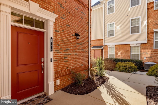 view of exterior entry featuring brick siding and central AC