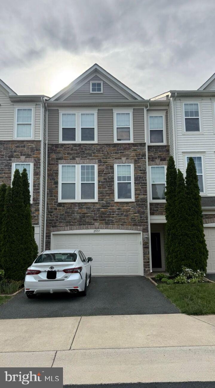 multi unit property featuring stone siding, asphalt driveway, and a garage