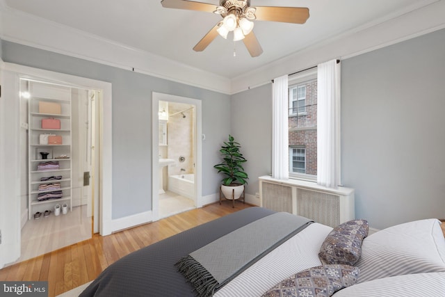 bedroom with radiator heating unit, wood finished floors, baseboards, ceiling fan, and ensuite bath