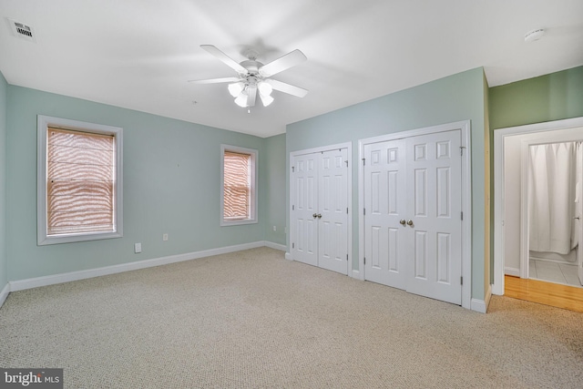 unfurnished bedroom with carpet, baseboards, two closets, and a ceiling fan
