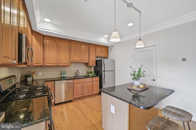 kitchen with stainless steel appliances, a sink, crown molding, light wood-style flooring, and backsplash
