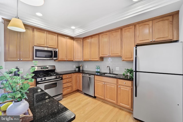 kitchen with appliances with stainless steel finishes, a sink, dark stone countertops, light wood-style floors, and ornamental molding