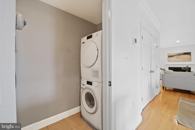 laundry room featuring stacked washing machine and dryer, crown molding, and baseboards